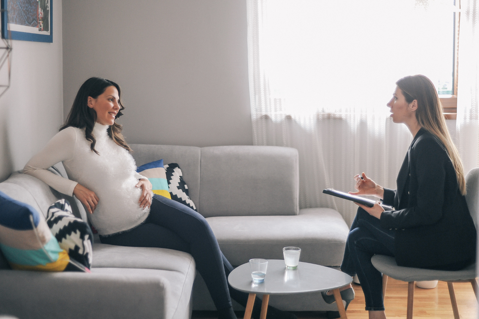 A pregnant person is sitting in their living room interviewing a newborn care specialist.