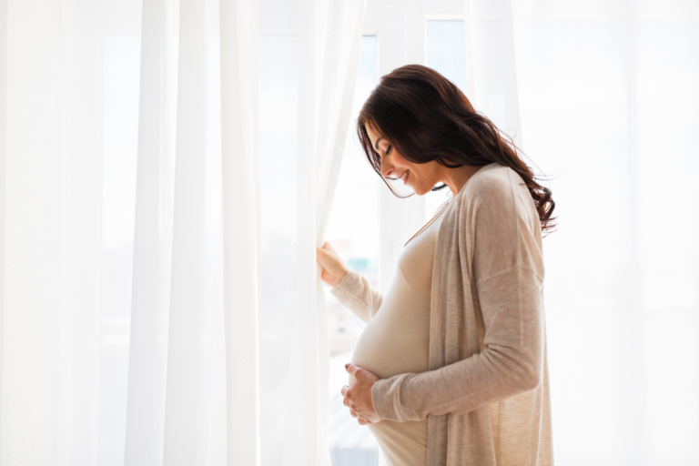 Pregnant woman standing by a window holding her baby bump